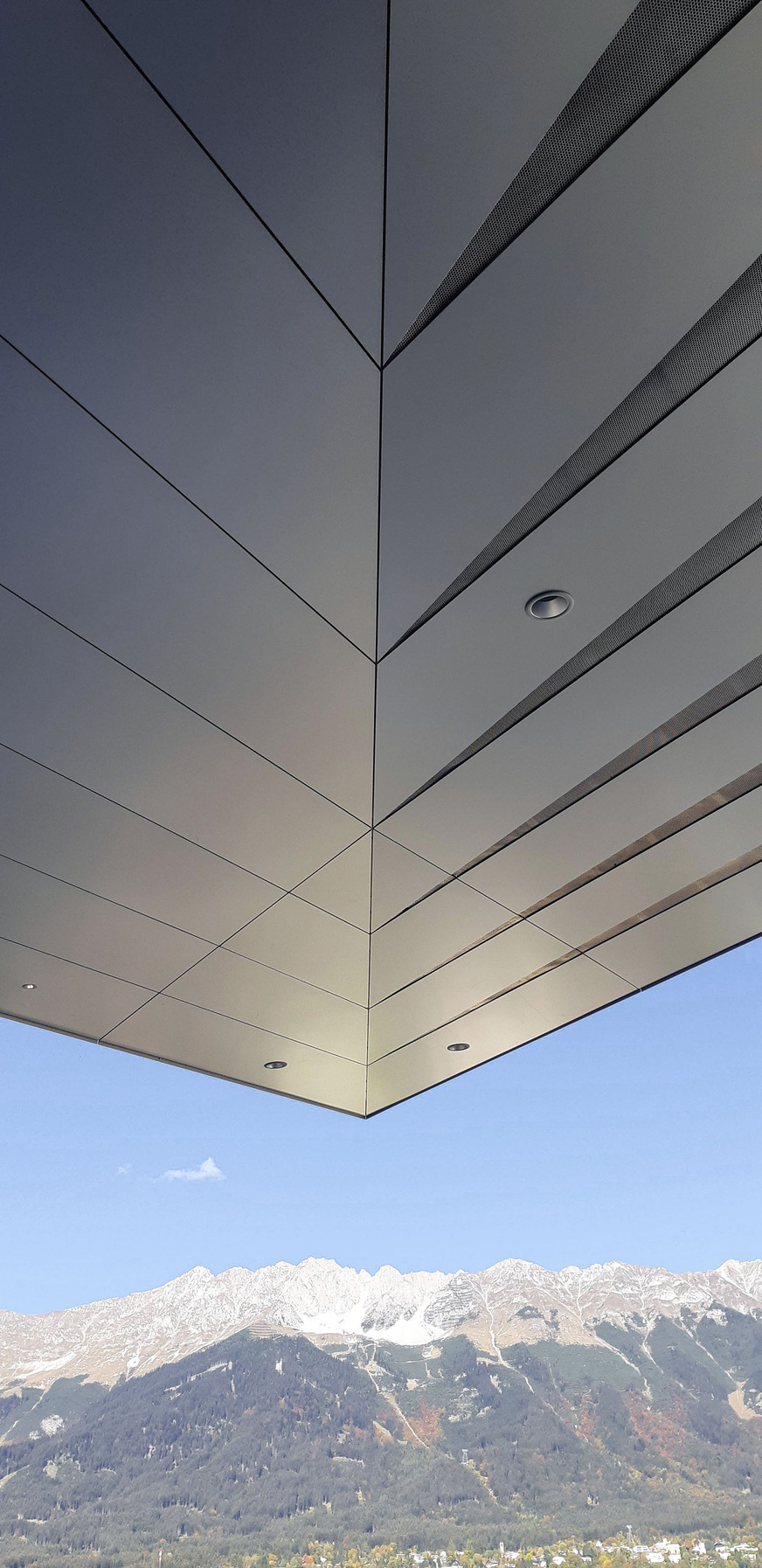 Perforierte Streifen aus Aluminium durch­brechen die Deckenbekleidung und laufen an der Gebäudeecke wie Pfeilspitzen aus