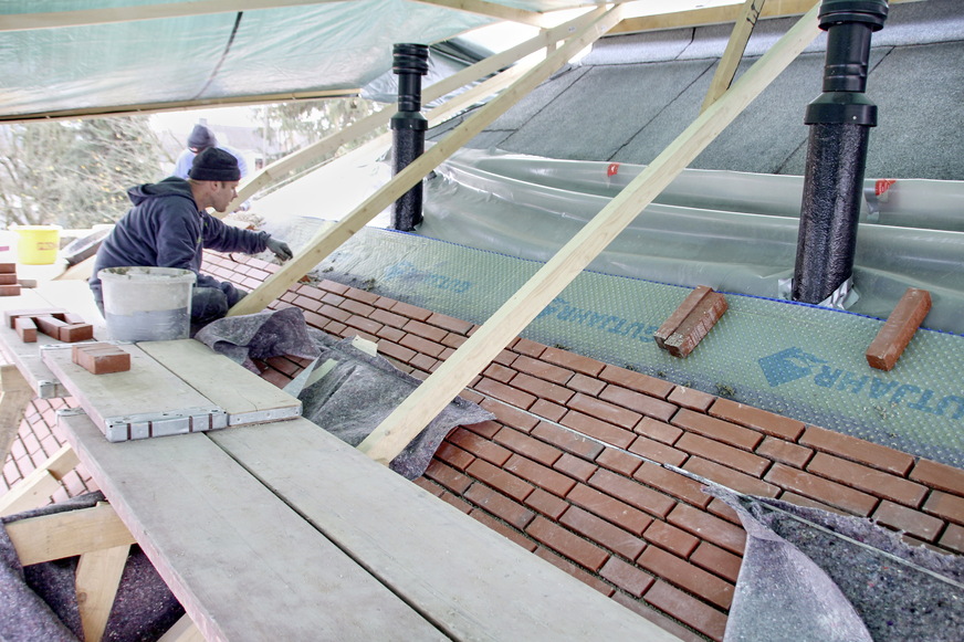 Maßarbeit auf dem Dach beim Verlegen der Klinkersteine im Mörtelbett