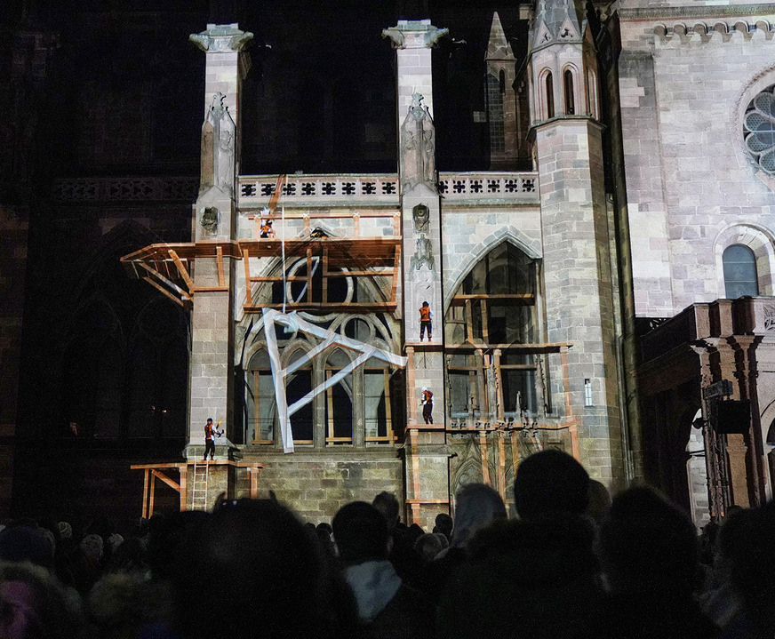 Vor den Augen zahlreicher Zuschauer gehen verschiedene Handwerker auf Holzgerüsten an der Fassade ihrer Arbeit nach