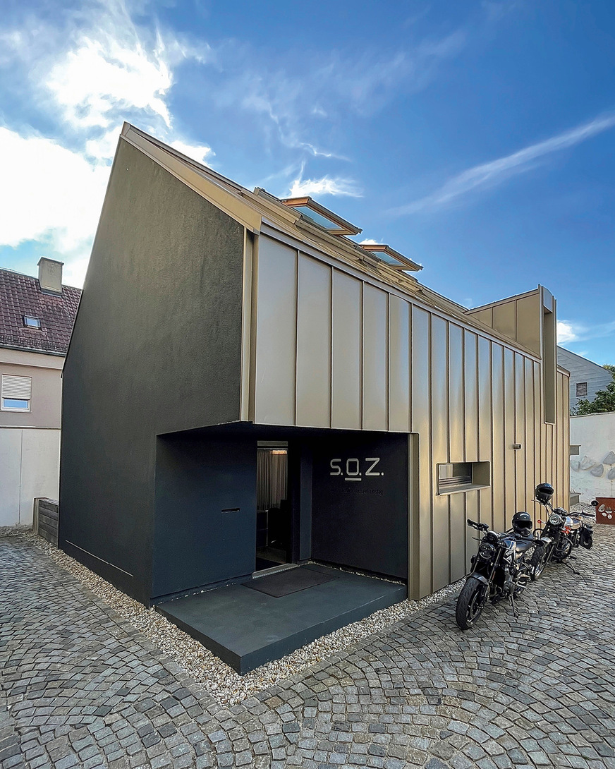 Spannende Kontraste entstehen durch anthrazitfarbene Putzflächen und sich anschmiegende Farbaluminiumbänder im Bronzefarbton