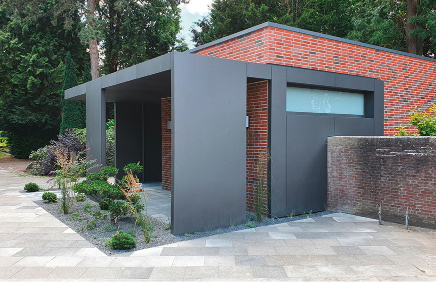 Das neue Toilettenhäuschen im Zusammenwirken zweier Materialien, rechts ein Stück der alten Mauer