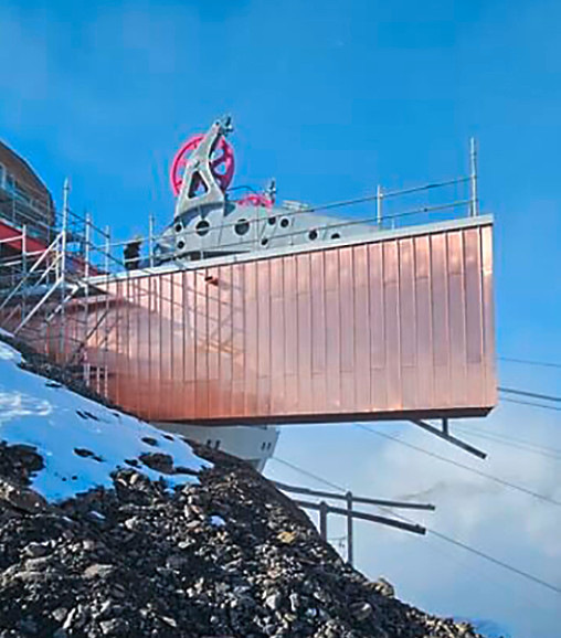 Riesige Umlenkräder ragen weit aus dem mit walzblankem Kupfer bekleideten Kubus