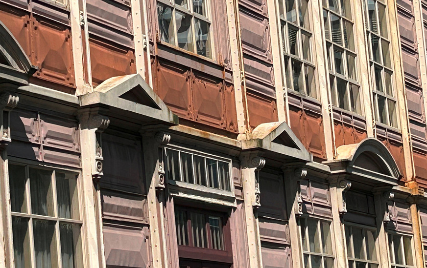 Zwischen Erd- und Obergeschoss verläuft ein braun gestrichenes Blechband