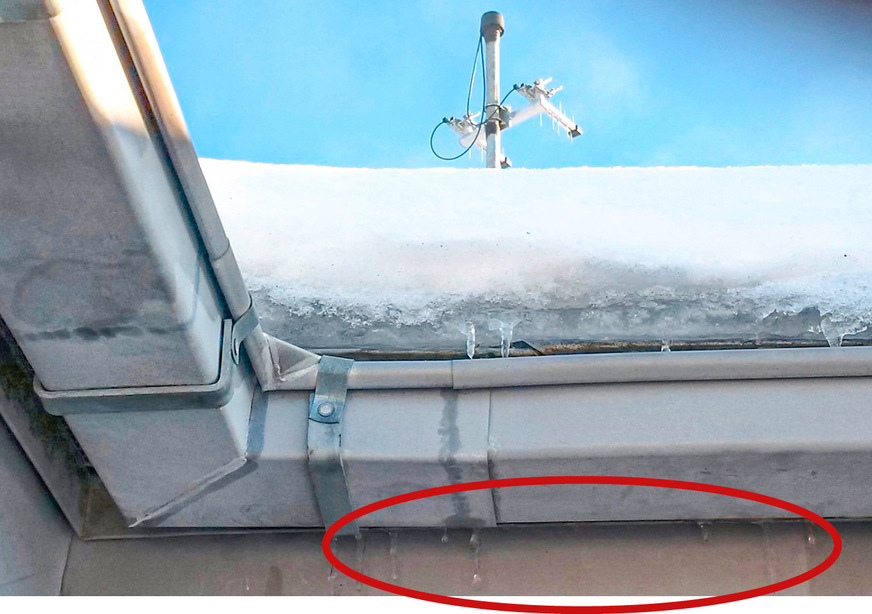 Eine dicke Eisschicht im Traufbereich eines ­Metalldaches. Leider sind die hinter der Rinne austretenden Wassertropfen bzw. sich bildende Eiszapfen nur schwach zu erkennen. Bei bestimmten klimatischen Bedingungen tritt aus der Belüftungsöffnung der Dachkonstruktion, hinter der Dachrinne, Wasser aus. Und zwar nur dann, wenn sich auf dem Dach Eis und Schnee befinden und Tauwetter herrscht. Bei allen anderen Wetterbedingungen ist das Dach dicht