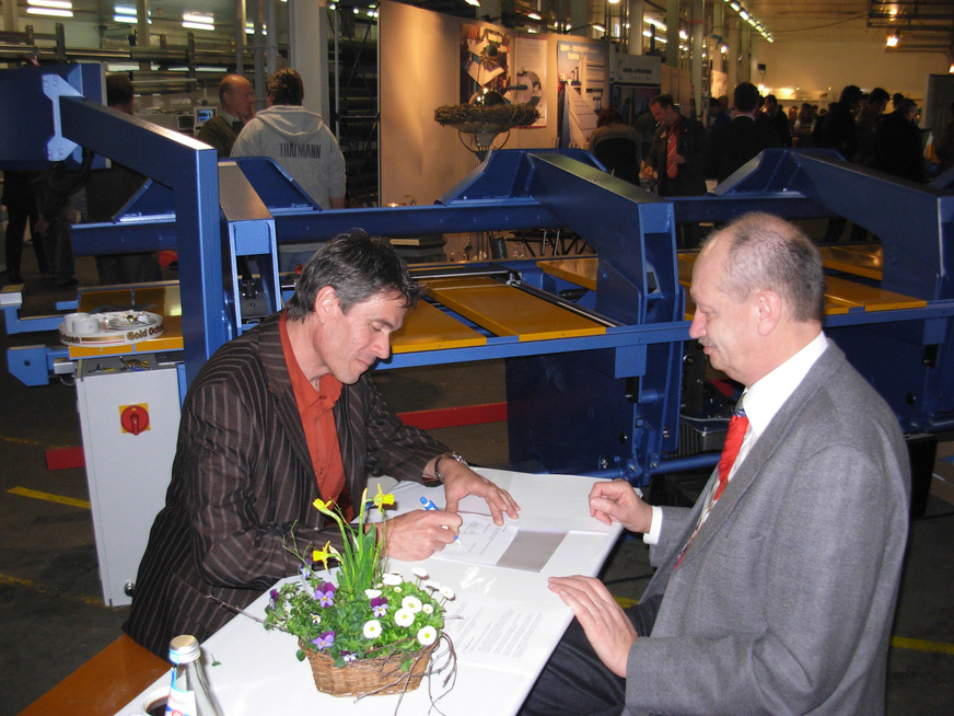 Unter den wachsamen Augen von Verlagsleiter Werner Ostertag unterzeichnet Andreas Buck auf der Hausmesse bei Kaufmann seinen Arbeitsvertrag als neuer Chefredakteur