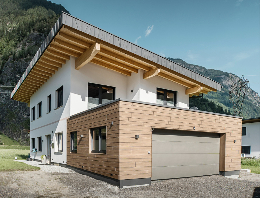 Das zweistöckige Gebäude kombiniert weiße Putzflächen mit Aluminiumbekleidungen an der geräumigen Garage