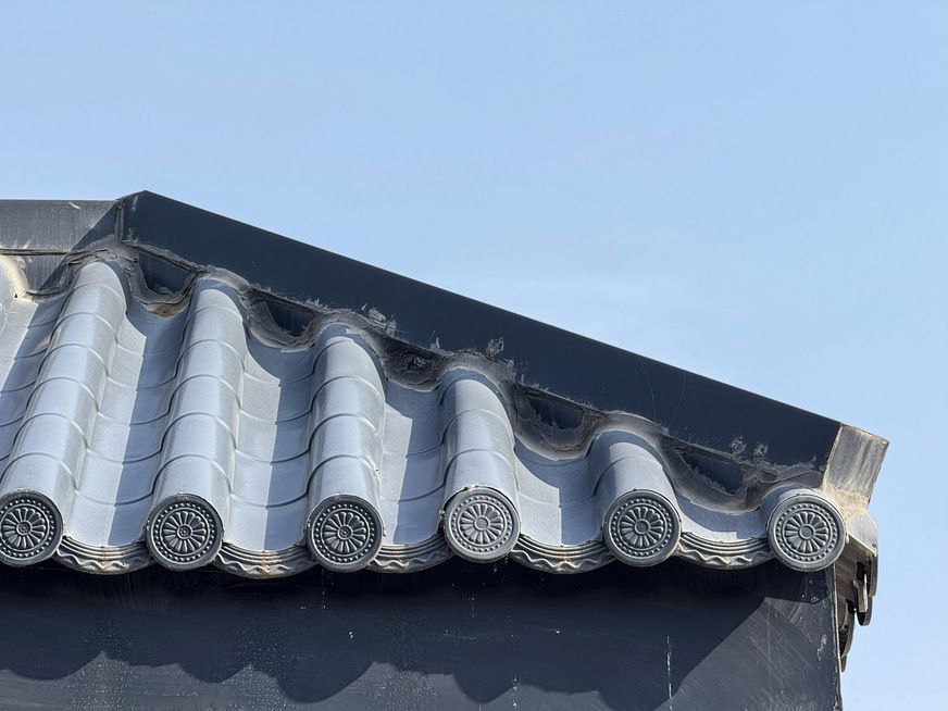 Industriell gefertigte Metalldachplatten&nbsp;im China-Ziegel-Look und mit geprägten Endkappen an der Traufe. Auffallend ist der massiv silikonierte Anschluss am Grat- bzw. First