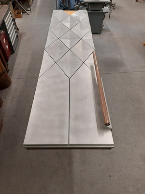 „Ursprünglich wollte der Architekt die Türe mit Messing verkleiden, das unten patiniert und nach oben hin (zum Licht) poliert wird. Da die Polierte Oberfläche aber nicht dauerhaft hell bleiben kann, sind wir im Gestaltungsprozess dann auf Zinnblech gekommen, das auch bei Verwitterung hell bleibt“