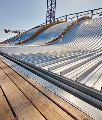 Für die geschwungene Dachform kamen die Kalzip-Stehfalzprofile 65/300 in der Oberfläche AluPlusPatina zum Einsatz. Aus zu 95 % recyceltem ­Aluminium hergestellt, sind die Profiltafeln in der Form anpassbar und ­zahlen auf das neue Nachhaltigkeitskonzept des Flughafens ein