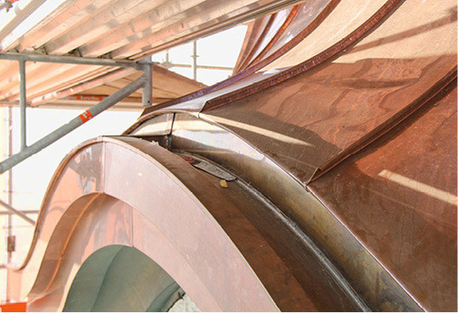 Die bogenförmig geschwungene Kastenrinne mit abgestuftem Gesims über einem der vier Zifferblätter der Turmuhr