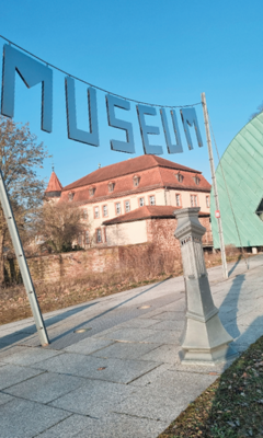 Gerne! Hier ein barrierefreier, themenrelevanter und zielgruppengerechter Alt-Text für das Bild: Alt-Text: Schriftzug „MUSEUM“ aus großformatigen Metallbuchstaben montiert an einer modernen Metallrahmenkonstruktion vor einem historischen Gebäude mit rotem Dach; zeigt hochwertige Fassadenintegration und Beispiele für professionelle Metallverarbeitung im Bestandbau. Begründung: Der vorgeschlagene Alt-Text stellt den Werkstoff, die technische Umsetzung (Metallrahmen), den architektonischen Kontext (Integration in historische Bausubstanz) sowie das Kernthema – fachgerechte Anwendung und Gestaltungsmöglichkeiten von Metallelementen an Fassaden – in den Vordergrund. Das ist für Betriebsinhaber, Fachwerker und Planende im Bereich Spengler-, Klempner-, Dachdeckerhandwerk relevant. - © Bild: EKKM