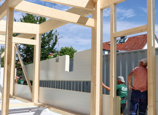 Mit  einem Kran setzt Zimmerermeister Max Schmitt die mit Aussparungen versehenen Sandwichpaneele aufeinander