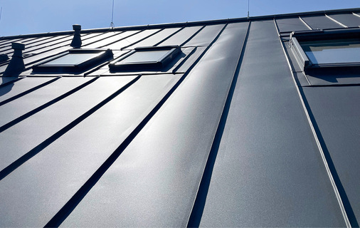 Deutliche Schar-Aufwölbung: Die Einfassung der Dachflächenfenster erfolgte mit industriell vorgefertigten, in die Fläche eingefalzten ­Eindeckrahmen. Die Querfalze sind als einfacher Falz ausgeführt und fachgerecht in die ­Doppelstehfalze eingebunden