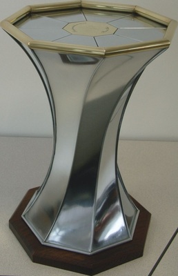 04 Achtteiliger Tisch Um 18° gedrehter Tischfuß, Tischplatte mit geschlitztem Rohr gefasstMaterial: Titanzink / Messing Verbindung: Falztechnik