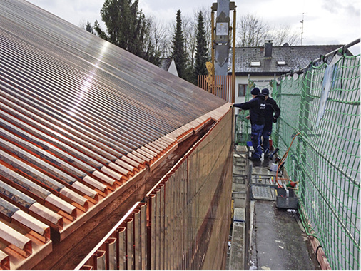 
Dachtechnik vom Feinsten: Kurze Profile wurden in die Kupferstäbe hineingeschoben. Die Mitarbeiter ziehen sie soweit wieder heraus, bis sie die Regenrinne verdecken. 
