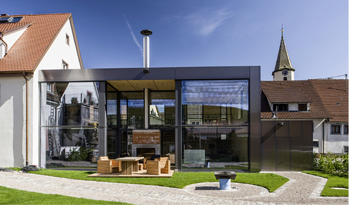 
Auf der Rückseite öffnet sich der Anbau großzügig zum Garten hin. In die Glasfront ist eine Terrasse mit Kamin integriert 
