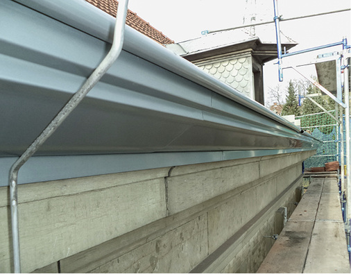 
Die Gesimsrinne aus Titanzink mit ihrem ausdrucksstarken Wulst schließt unmittelbar an den Sandstein an und ist dadurch in der Ansicht von unten kaum als eigenständiges Bauteil wahrnehmbar 



