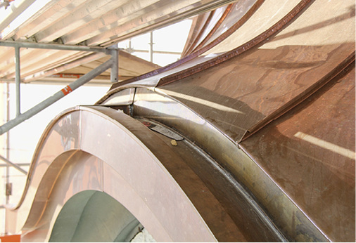 



Die bogenförmig geschwungene Kastenrinne mit abgestuftem Gesims über einem der vier Zifferblätter der Turmuhr 
