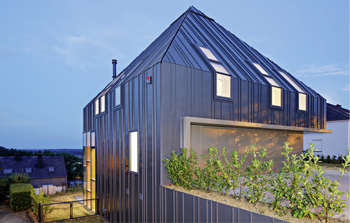 



In der Abendstimmung unterstreichen die Lichtflächen der Fenster im Traufknick den Zusammenhang zwischen der Fassade und dem Dach
