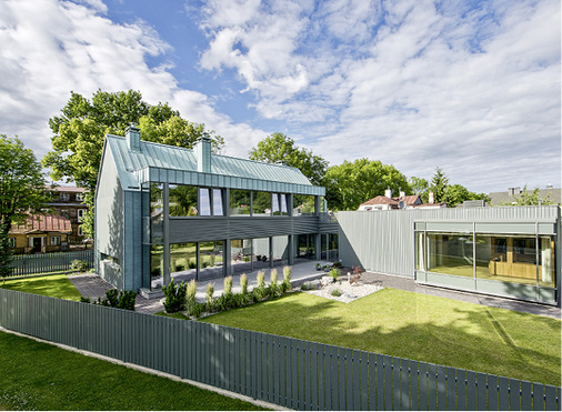 
Zum Garten hin öffnet sich der geschlossene, geometrische Baukörper mit einer Glasfront. Die horizontale Struktur der Fassade bildet einen Kontrast zu den Längsfalzen an Dach und Seitentrakt



