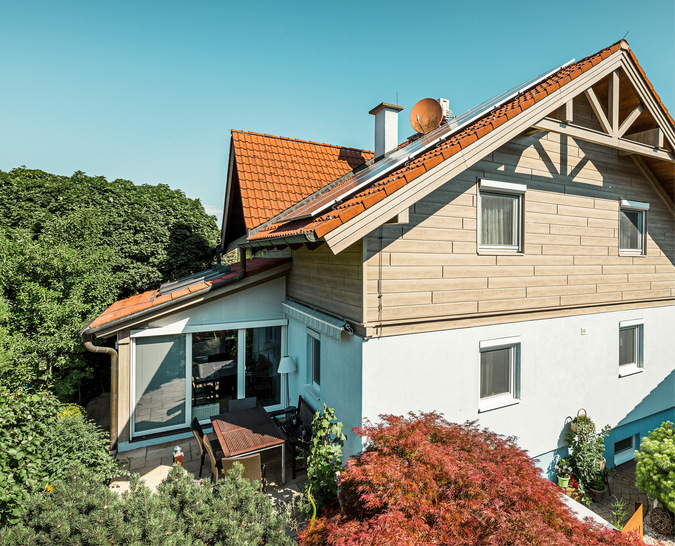Die Fassade kombiniert weiß verputzte Flächen mit Aluminium-Sidings in der Holzoptik „Eiche beige-grau“
