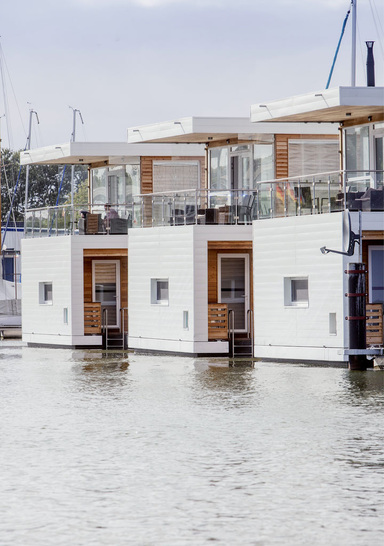 Beim schwimmenden Ferienhaus Floating 100 handelt es sich um ein auf einem Schwimmponton in Holzrahmenbauweise aufgebautes, zweigeschossiges Gebäude mit großer Dachterrasse. Die Tragwerkskonstruktion fur Wande und Decken besteht aus einer Holz- oder Stahlrahmenkonstruktion mit einer darauf aufgebrachten OSB-Platte. Diese wird mit einer dampfdiffusionsoffenen Unterspannfolie dicht bekleidet. Darauf kommt eine Tragkonstruktion, an der GFK-Sandwich- oder Aluminium-Fassadenelemente befestigt werden. Fallrinnen und Entwasserungen fur das Dach und die Terrasse im OG werden nicht sichtbar in der hinterlufteten Fassade im Bereich des Pontons abgefuhrt