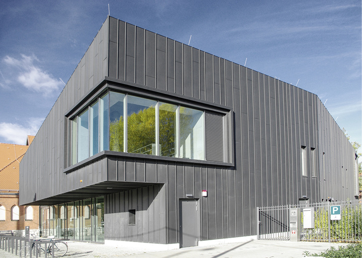 



Die Gebäudehülle aus vorpatinierten Zinkprofilen prägt das Erscheinungsbild des Neubaus
