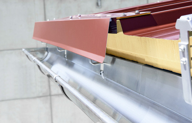  Das Rinnenhaken-Set von Zambelli ermöglicht es, Dachrinnen direkt an der Deckschale des Sandwichpaneels zu befestigen. Ein zusätzliches Prallblech verhindert das Überschießen von Regenwasser