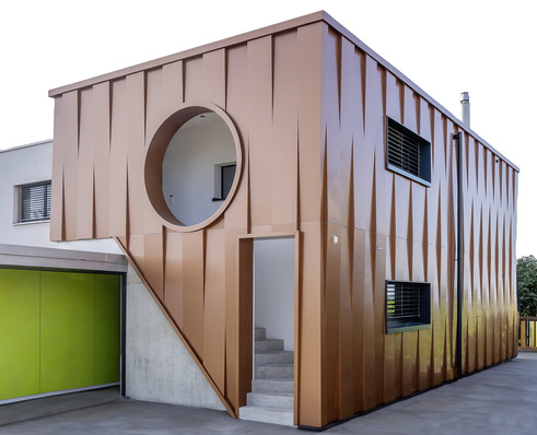  Die schmalen aus- und einspringenden Fassaden-­Kassetten beleben den Ausdruck des ­Anbaus. Die runde Fassadenöffnung wurde in der Werkstatt mehrteilig hergestellt und erst bei der Montage zusammengefügt