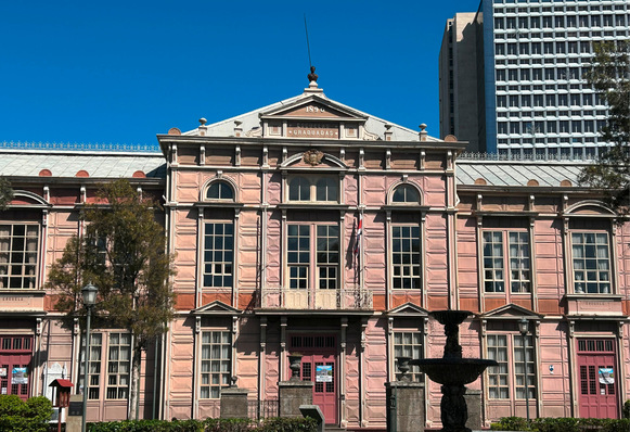 Alt-Text: „Detailaufnahme einer historischen, rosafarbenen Fassade mit kunstvollen Metallverzierungen, illustriert als inspirierendes Beispiel für innovative Fassadengestaltung im Kontrast zu angrenzenden modernen Hochhausstrukturen.