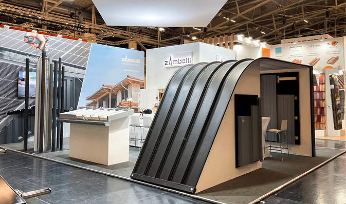 Alt-Text: „Messestand mit innovativen Dachmaterialien und Solarpanelen, präsentiert unter einer modernen schwarzen Bogenkonstruktion, hervorgehoben als Bau- und Architekturtrend für Spengler und Dachdecker. - © Bild: Zambelli