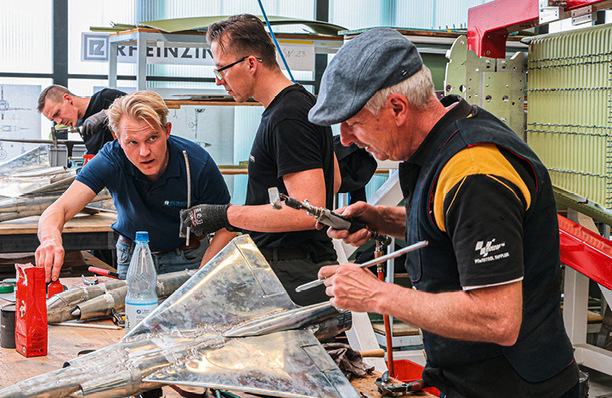 „Handwerkerteam in einer Werkstatt bei der Bearbeitung von Metallteilen für den Flugzeugbau mit modernen Verarbeitungstechniken. - © BAUMETALL