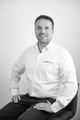 Sicher, hier ist ein optimierter Alt-Text für das beschriebene Bild: „Facharbeiter im weißen Shirt mit Firmenlogo lächelt, zeigt Vertrauen und Expertise in der modernen Metallverarbeitungstechnik.“ Dieser Alt-Text spiegelt die Professionalität und das Fachwissen wider, die von der Zielgruppe in der Gebäudetechnikbranche geschätzt werden. - © VM Building Solutions